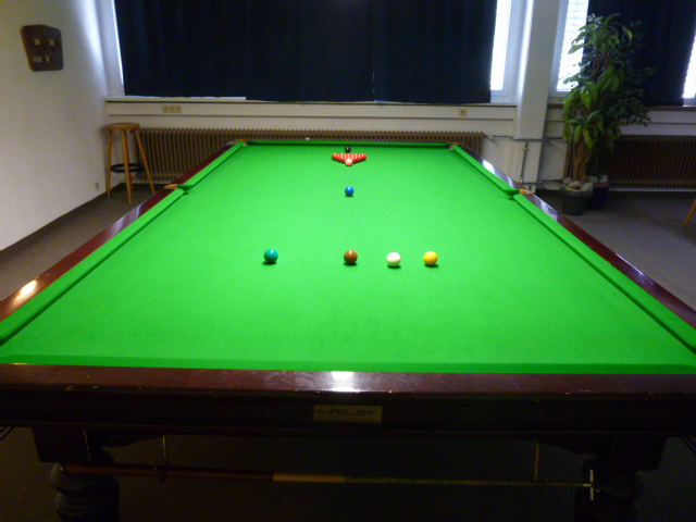 Ein Snookertisch vor Beginn eines Frames. Die 15 roten Kugeln sind als Dreieck aufgebaut, die 6 farbigen Kugeln befinden sich auf ihren Punkten und der weiße Spielball liegt im Halbkreis.
